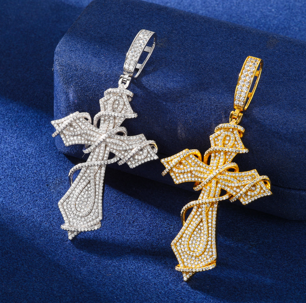 Two cross-shaped pendants, one silver and one gold, on a blue fabric background.